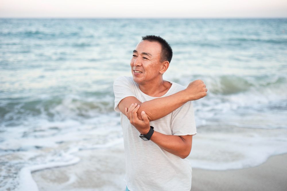 man by the beach coastal stretching arms